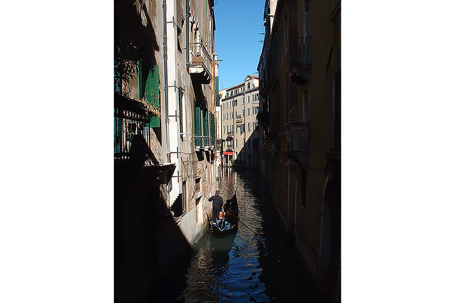 Canal in Venice with gondola in foreground between rows of buildings in light and shadow.