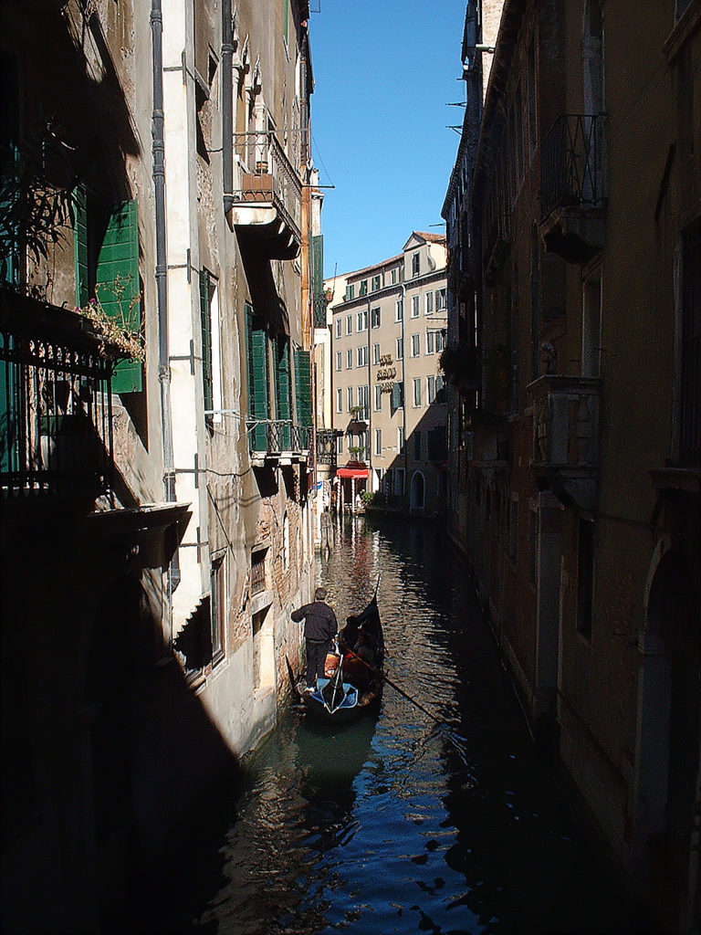 Canal in Venice with gondola in foreground between rows of buildings in light and shadow.