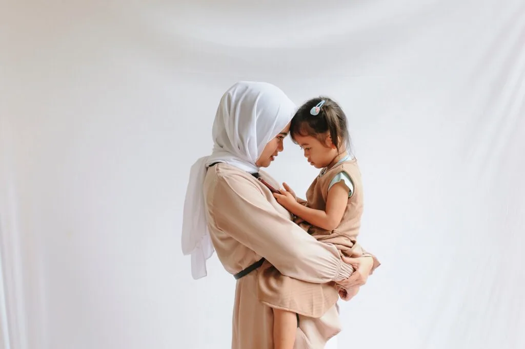 Portrait image of a mother holding her daughter posed against a soft white background.